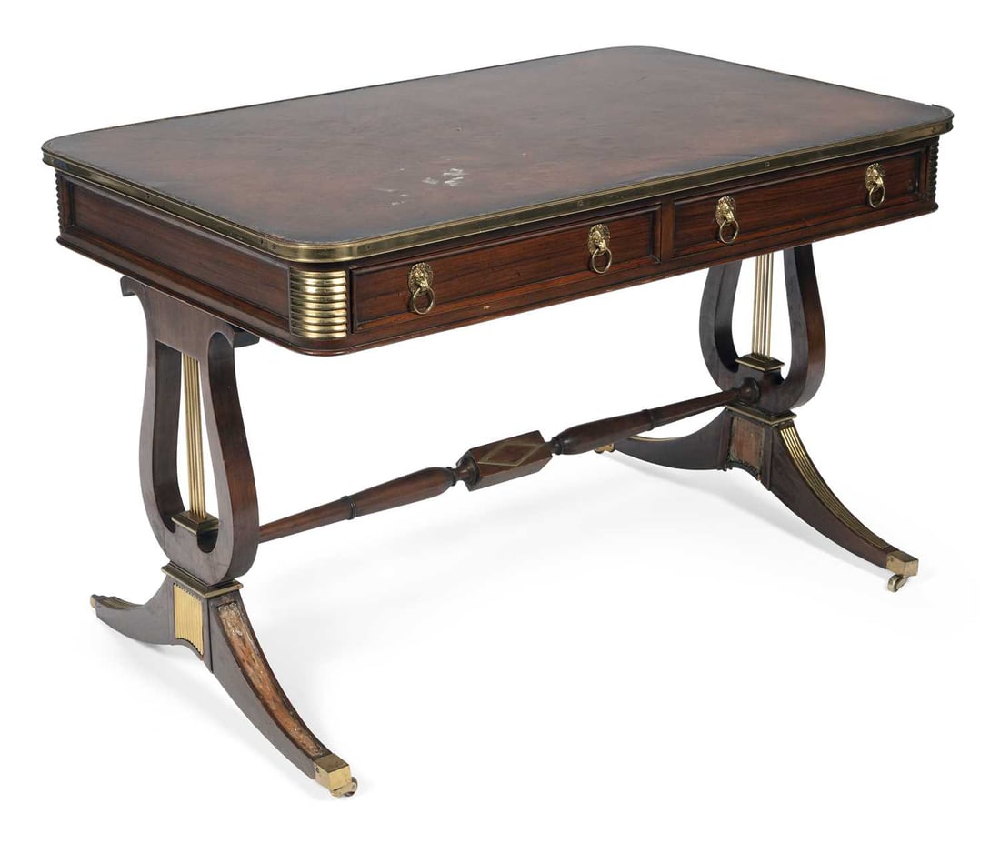 A REGENCY BRASS INLAID ROSEWOOD LIBRARY TABLE: the rectangular top inset with a tooled leather writing surface within a brass edge moulding, the rounded corners with gadrooned brass mounts, above two frieze drawers with cast lion mask ring handles