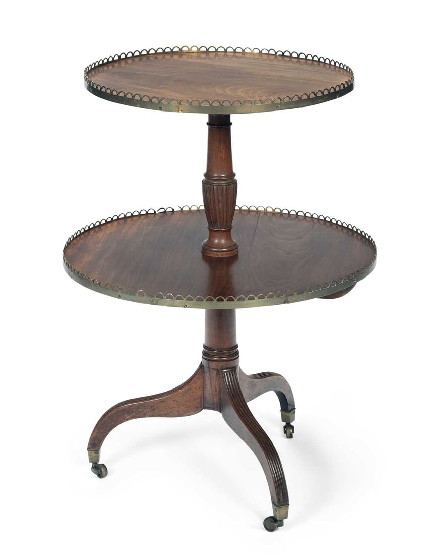 A REGENCY MAHOGANY TWO TIER DUMB WAITER: the graduated circular tiers within pierced brass galleries, on a turned and reeded baluster column, the tripod base with reeded downswept legs terminating in brass caps and castors. 88cm high,