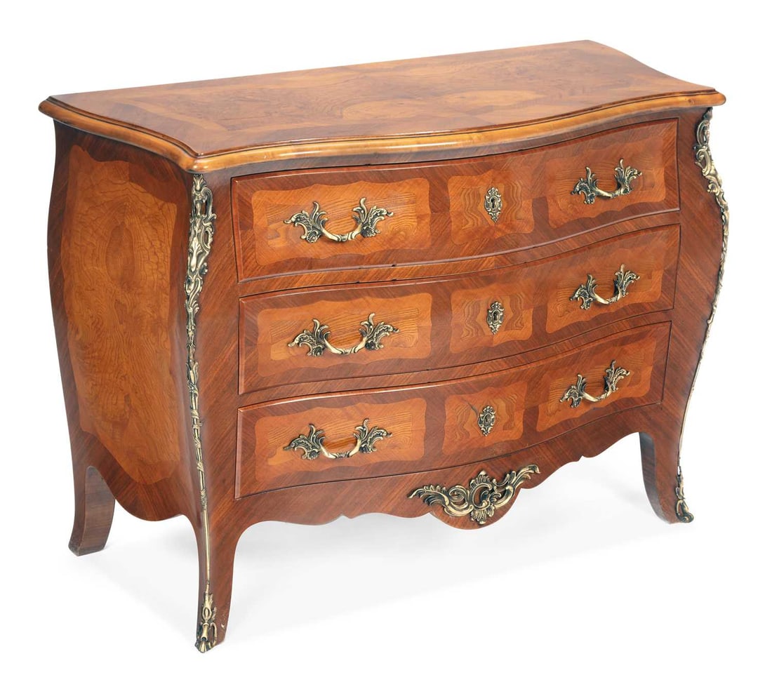 A WALNUT BOMBE COMMODE: in the Louis XV taste, the shaped serpentine top veneered in burr walnut within crossbanding, above three long graduated drawers with gilt-metal handles and escutcheons, the angles and shaped apron ap