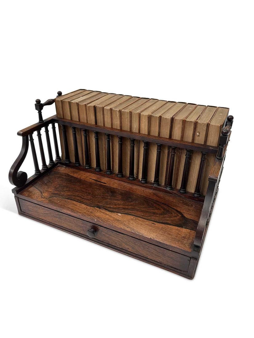 A VICTORIAN ROSEWOOD BOOK RACK: the rectangular platform with a single frieze drawer, flanked by turned spindle galleries between scroll end supports with turned carrying handles, together with seventeen volumes of The Waverley Nove