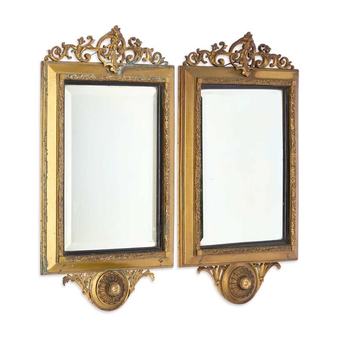 A PAIR OF GILT-METAL MOUNTED WALL MIRRORS LATE 19TH CENTURY: in the Empire taste, each with a rectangular bevelled plate within an ebonised slip and a moulded frame applied with a foliate band and gilt corner blocks, surmounted by a pierced scrolling foliate cr