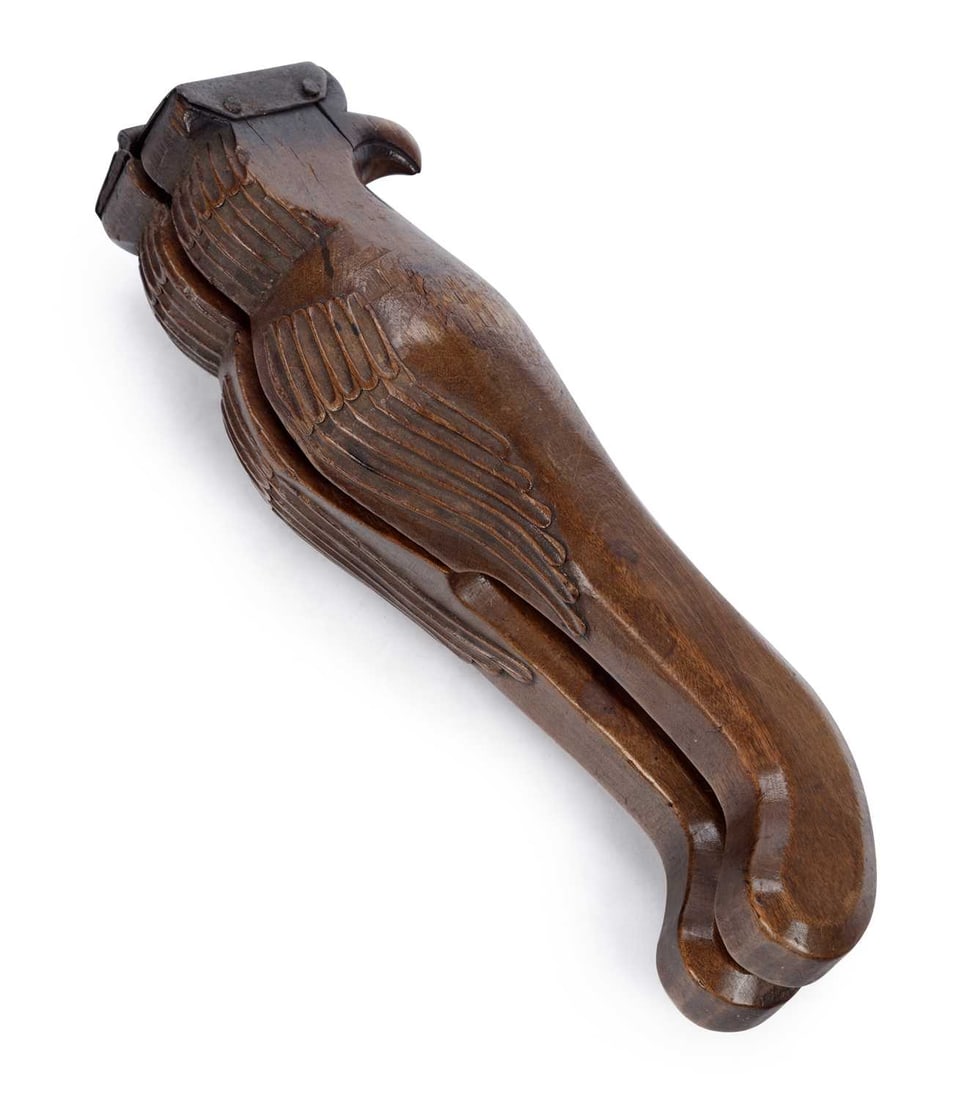 AN 18TH CENTURY CARVED WOOD LEMON SQUEEZER: modelled as a bird with a hooked beak and carved wings, the hinged arms with iron mounts to the head, one arm hollowed with a circular bowl pierced for the juice, the other carved with a stylised flow