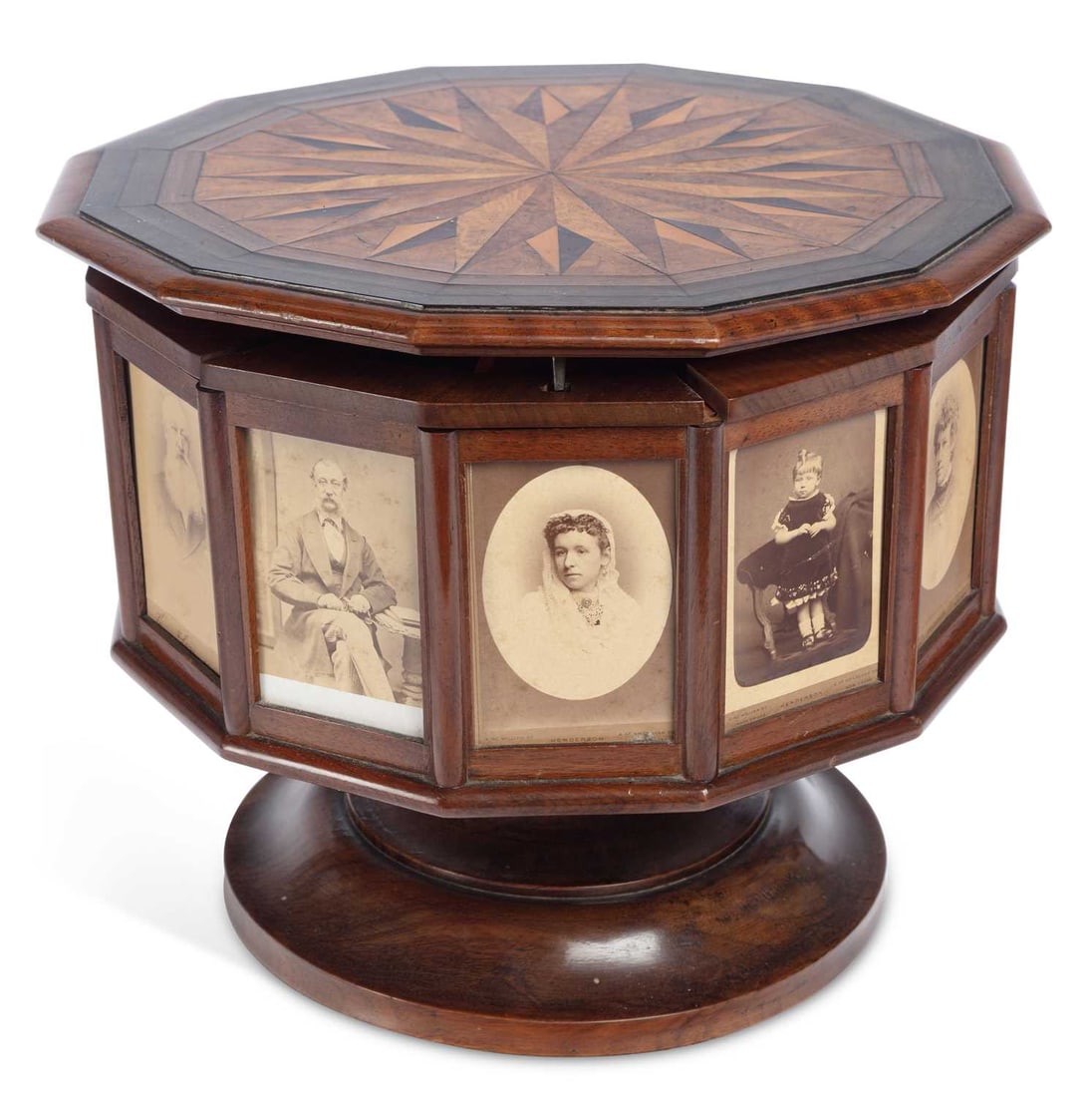 A VICTORIAN REVOLVING PHOTOGRAPH AND WORK BOX: of polygonal form, the hinged cover inlaid in specimen woods with a radiating star within crossbanded borders, the sides with glazed panels enclosing carte de visite portraits, several with