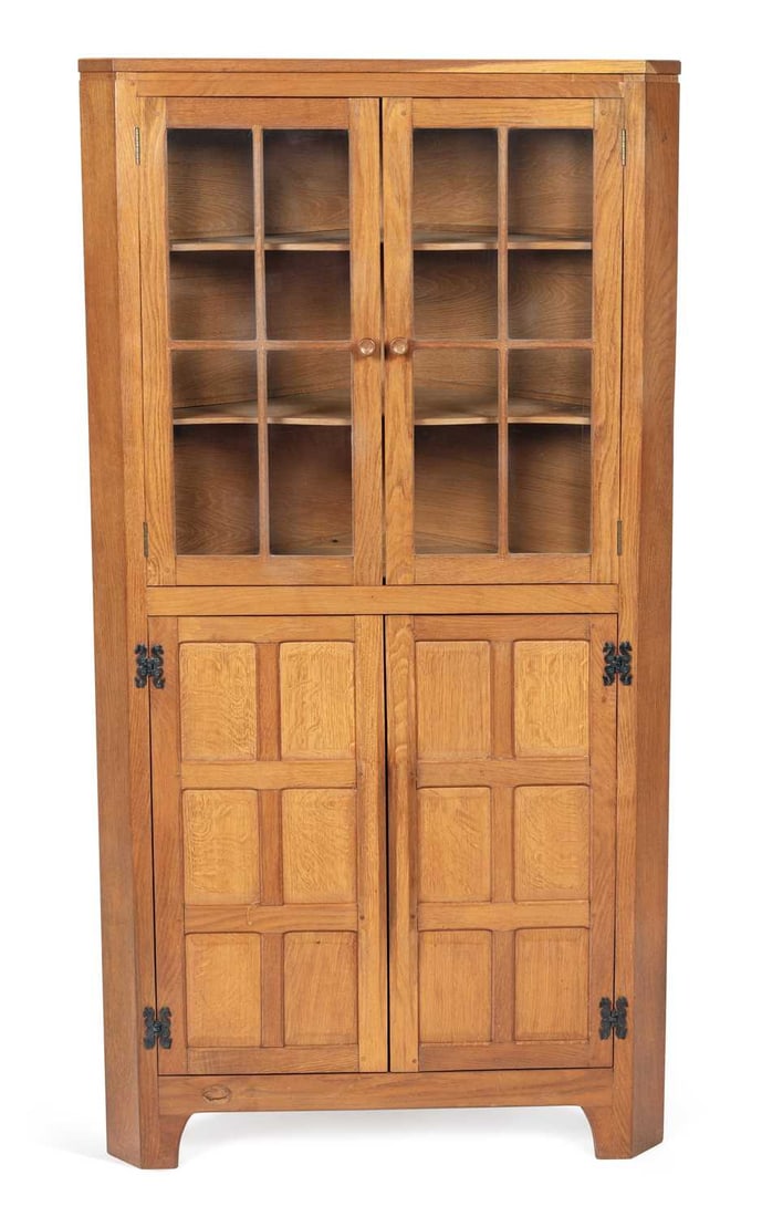 DEREK SLATER A FISHMAN OAK CORNER CABINET: the moulded cornice above a pair of glazed doors enclosing shelves, the base with a pair of panelled doors on wrought iron strap hinges, the apron carved with the fish signature, the adzed surfaces