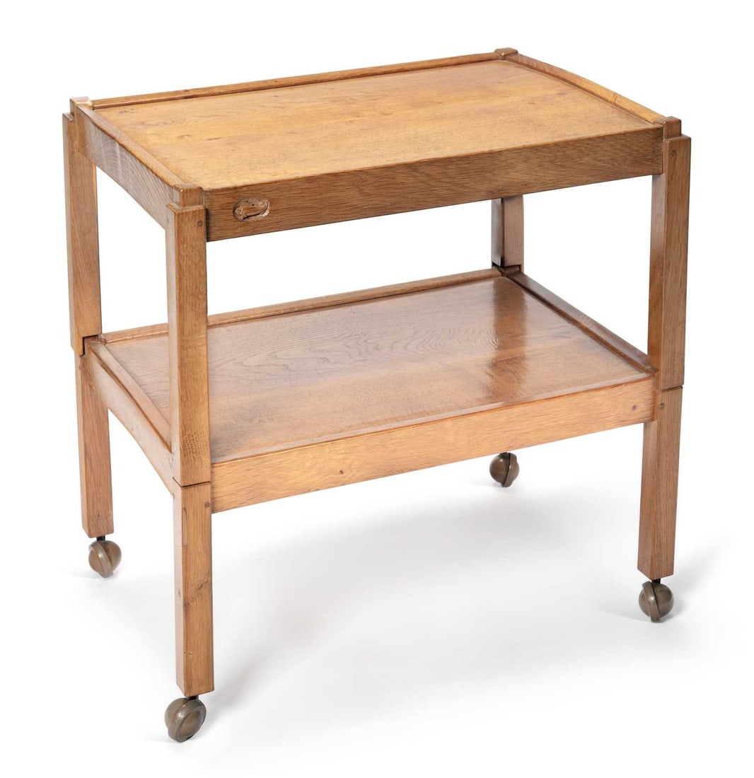 DEREK SLATER A FISHMAN OAK TEA TROLLEY: the adzed rectangular top within a raised gallery above a matching under tier, the frieze carved with the fish signature, raised on square legs with castors. 65.5cm high, 64cm wide, 45cm deep