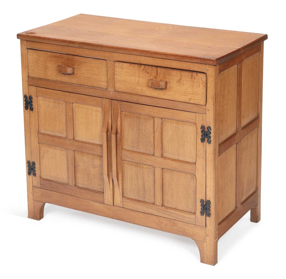 DEREK SLATER A FISHMAN OAK SIDEBOARD: the adzed rectangular top carved to one corner with the fish signature, above two frieze drawers with shaped handles and a pair of panelled cupboard doors on wrought iron strap hinges, raised on shape