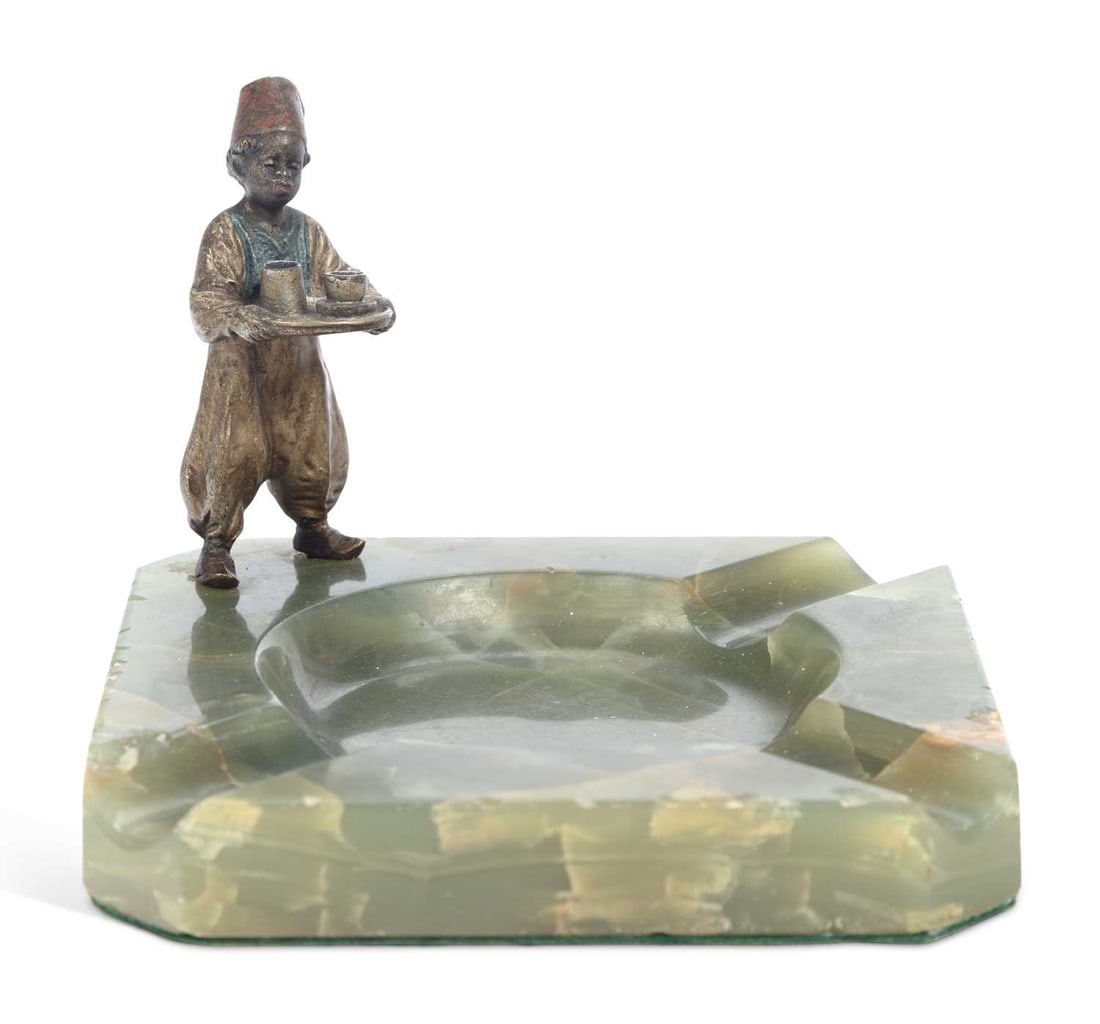 AN AUSTRIAN COLD PAINTED BRONZE AND ONYX ASHTRAY EARLY 20TH CENTURY: AN AUSTRIAN COLD PAINTED BRONZE AND ONYX ASHTRAY EARLY 20TH CENTURY mounted to one corner with a figure of an Arab boy in a fez and waistcoat carrying a tray of coffee cups, on a canted square green