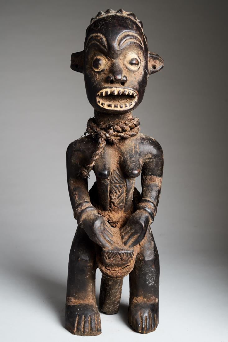 African Female Statue playing Drums: A statue of a female playing a drum that is clasped between her kneesThe raised eyebrows, wide open eyes and large mouth with sharp white teeth, give this figure an agressive look. Approx. 48x14x12 cm