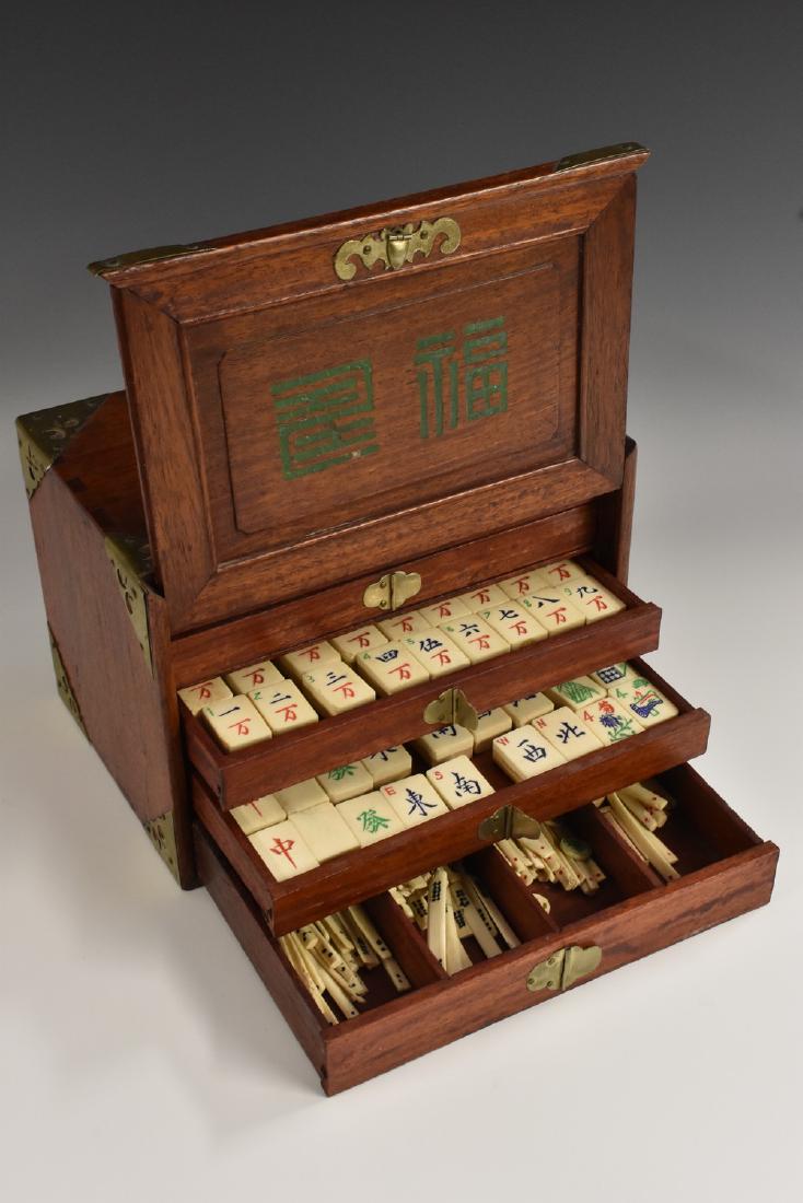 A Chinese hardwood mah jong cabinet, brass carrying: A Chinese hardwood mah jong cabinet, brass carrying handles above a sliding cover enclosing five graduated drawers of tiles, 24cm wide; Peterson (Henry), Mah John Simplified: Elementary & Advanced, Ru