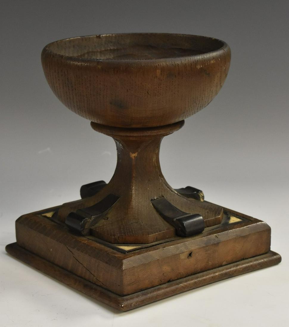 An oak offertory bowl, the spreading socle inlaid with: An oak offertory bowl, the spreading socle inlaid with bond and applied with ebony dressings, square base, 15cm high, 19th century or earlier