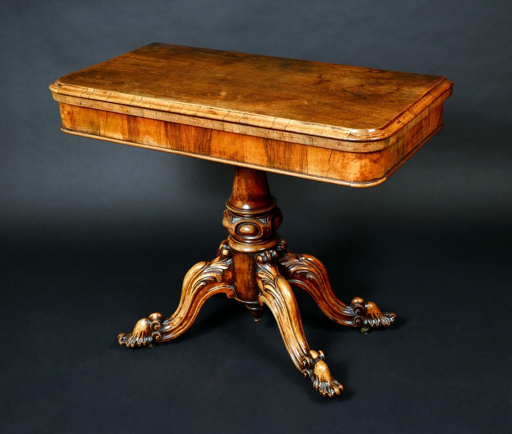 A William IV rosewood rounded rectangular card table,: A William IV rosewood rounded rectangular card table, folding top enclosing an inset baize lined playing surface, turned column, cabriole legs boldly carved with acanthus scrolls, 75cm high, 92cm wide