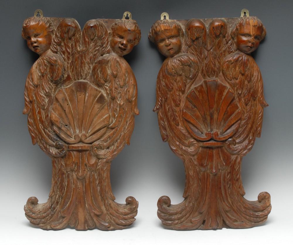 A pair of English Baroque limewood architectural: A pair of English Baroque limewood architectural carvings, each carved with a pair of winged putto and centred by shells, acanthus-capped leafy scrolls to apron, 49cm high, 27cm wide, c. 1695-1700