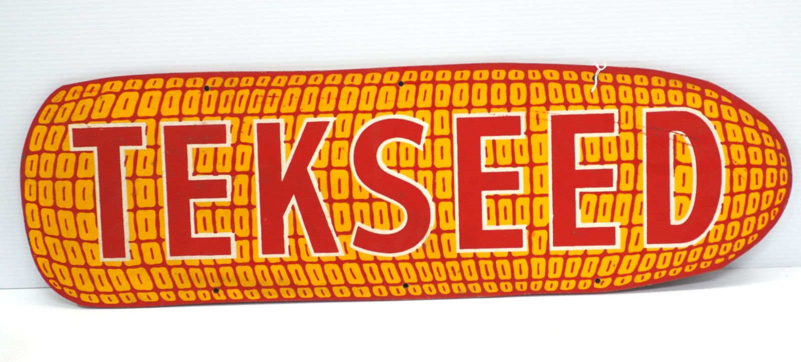 Tekseed sign: 33"x10" masonite Tekseed sign -Good ***These items are not located at the Chupp Auctions facility and will not be available for preview until April 1. As a result, some questions/info requests will no
