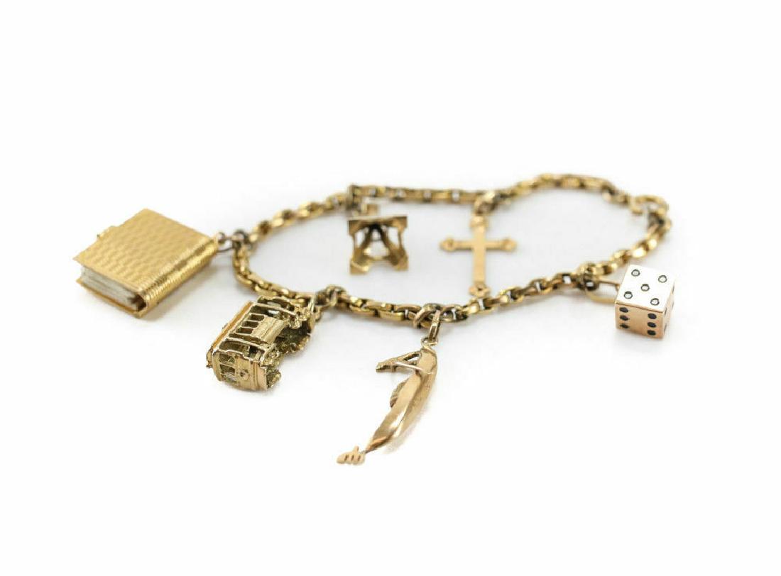 Mixed 14k Yellow Gold Charm Bracelet: 14k yellow gold charm bracelet. The bracelet consists of 6 charms including a cross, the Eiffell Tower, a book, a trolly, a man on a boat, and a dice cube. Marked to the pendent hooks. Weight Approx.,