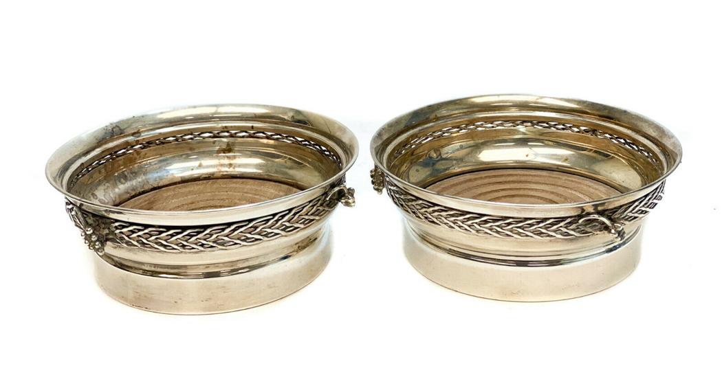 Cartier Sterling Silver Wine or Champagne Bottle: Pair Cartier sterling silver wine or champagne bottle coasters, Mid Century. Pierced weave texture to the rim with applied grapes with a wooden base. Cartier Sterling silver marks to the underside. We