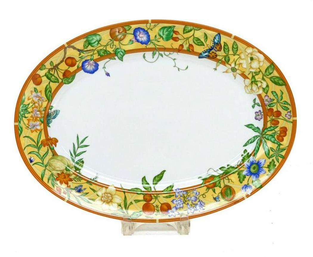 Hermes Porcelain Large Oval Platter in La Siesta: Hermes Paris porcelain large oval serving tray platter in La Siesta. Orange and yellow rims with butterflies, fruits, and flowers. Marked "Hermes" to the edge. Hermes mark to the underside along with