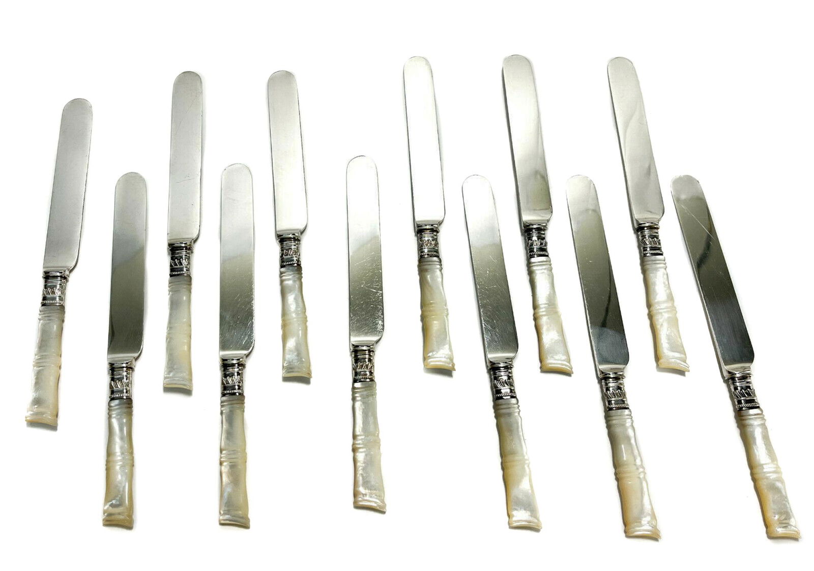 12 Mother of Pearl Handled Knives: 12 American steel and Mother of Pearl fruit or dessert knives, circa 1920. Mother of Pearl carved to resemble bamboo. Silver plate ferrules, blades marked Duhme & Co. Cincinnati. With rolled flatware