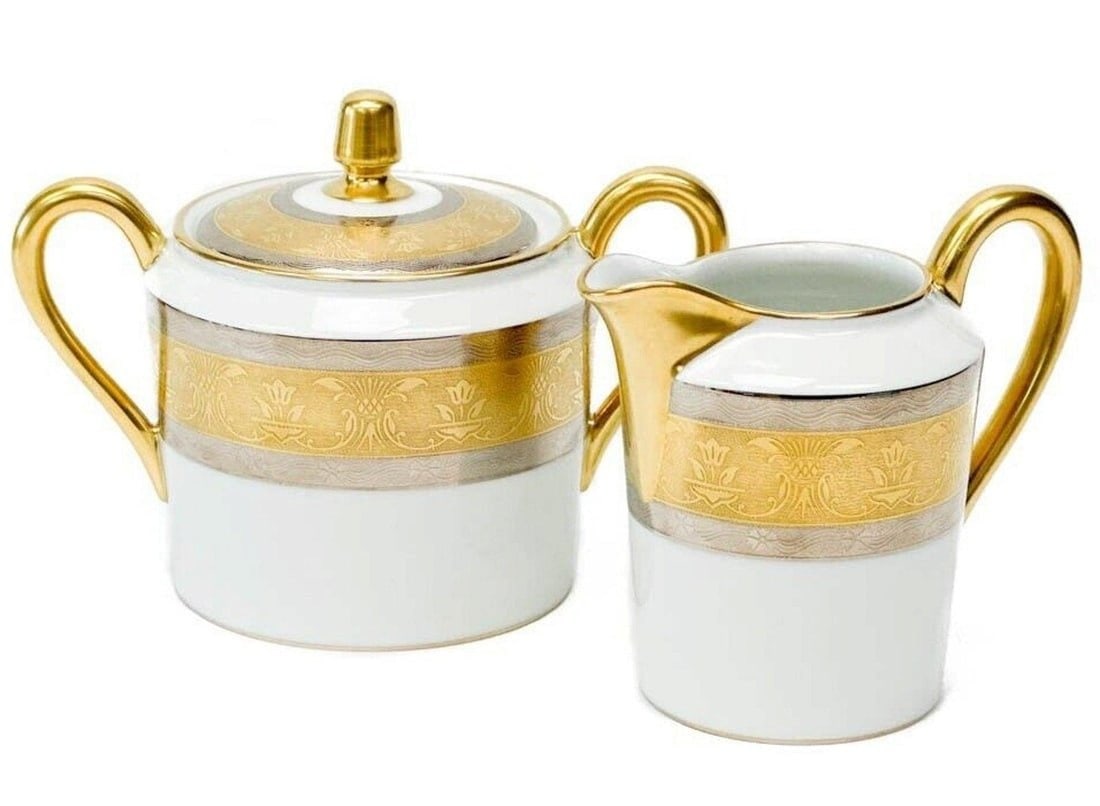 2pc Christofle France Gilt & Platinum Banded Porcelain Cream & Sugar in La Paiva: Christofle France porcelain creamer and lidded sugar bowl in La Pavia. A white ground to center, gilt to the edge and with platinum bands to the rim with floral designs. Gilt to rims and handles. Unde
