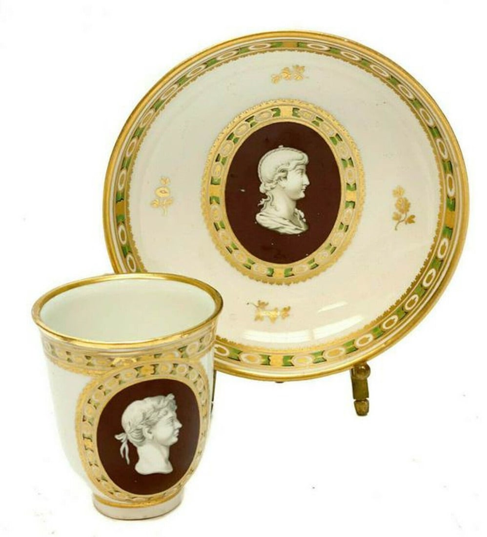 Imperial Royal Vienna Manufactory Porcelain Portrait Cameo Cup & Saucer 1798: Imperial Royal Vienna porcelain cameo cup & saucer, circa 1900. The central area of the cup and saucer depict a cameo portrait of Greek figures, one wearing a laurel leaf wreath. Gilt floral accents. 