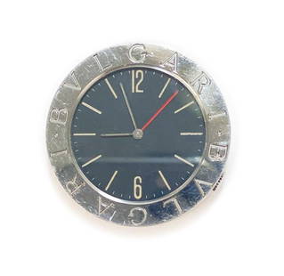 Bvlgari Travel Clock: A small Bulgari round travel clock AB 01-SS / F 45996. Marked Bvlgari to the face of the rim. Marked to the verso. A back stand. With arabic indexes and numbers and a quartz movement. Weight: Approx.