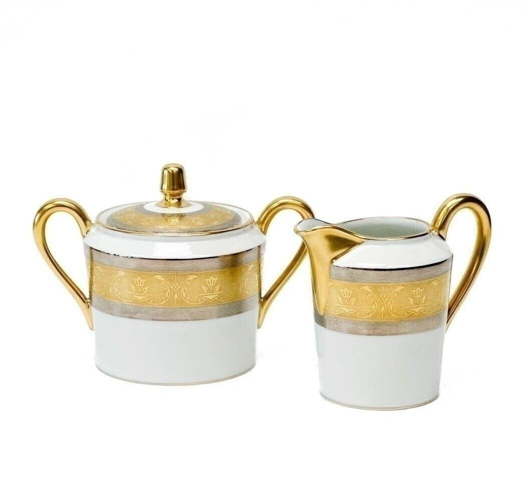 2pc Christofle France Gilt & Platinum Banded Porcelain Cream & Sugar in La Paiva: Christofle France porcelain creamer and lidded sugar bowl in La Pavia. A white ground to center, gilt to the edge and with platinum bands to the rim with floral designs. Gilt to rims and handles. Unde