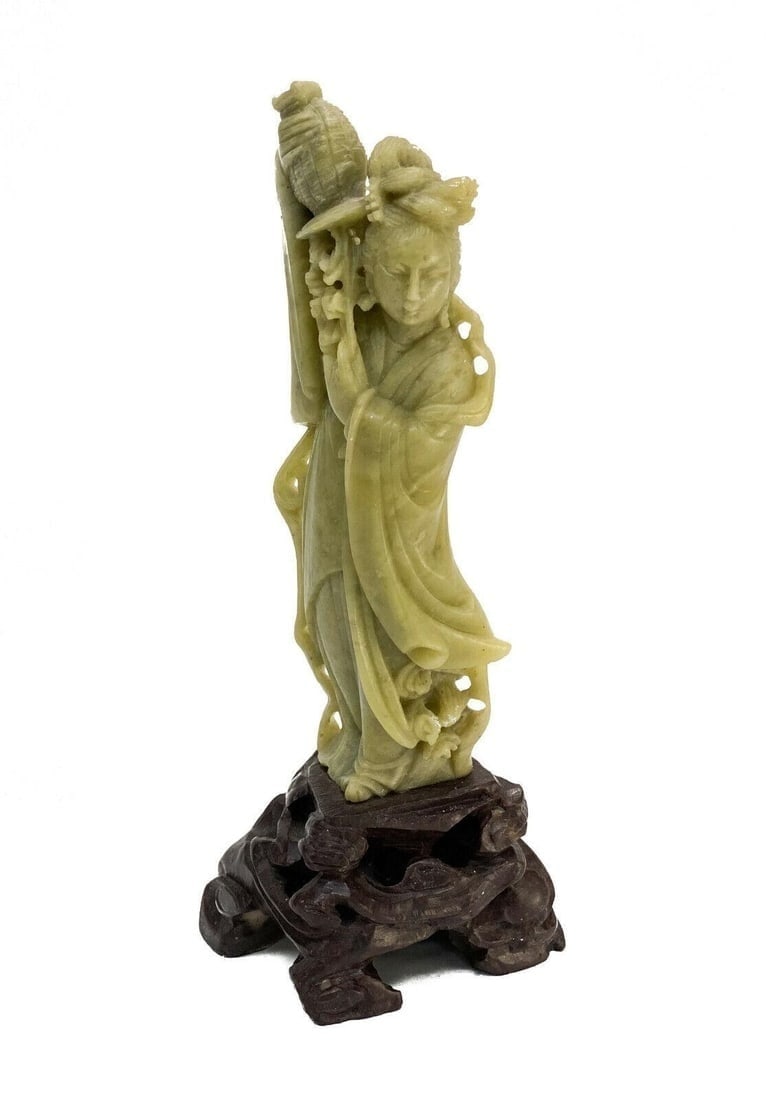 Chinese Carved Green Stone Figurine- Woman Holding Vase: Chinese carved green stone figurine, 20th Century. The figure depicts a Chinese woman in traditional garbs and holding a wicker base upside down and pulling flowers. Mounted to a wooden base. The ston