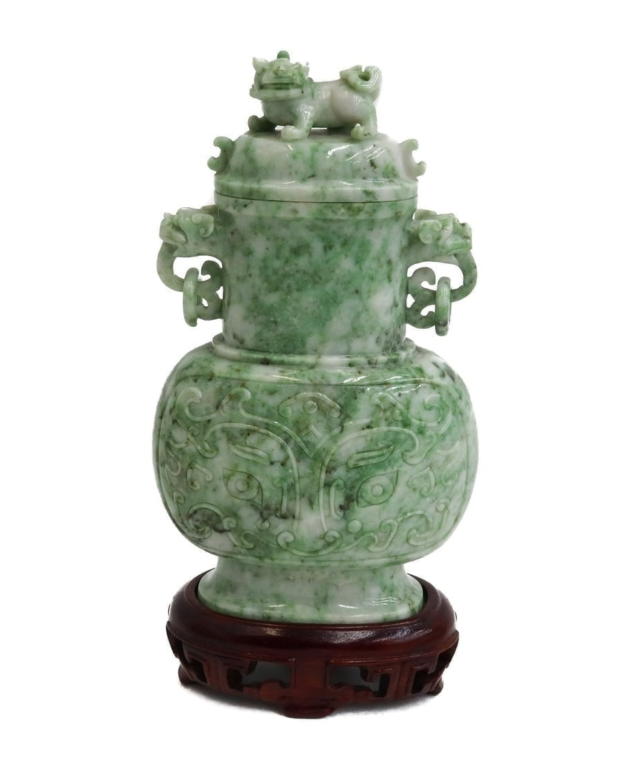 Chinese Carved Green Hardstone Decorative Urn on Base: Chinese Carved Green Hardstone Decorative Urn on Base. Figural foo dogs to the handles and finial with an engraved archaic figural masks to body. Mounted on a wood base. Weight Approx., 2 lbs Measures