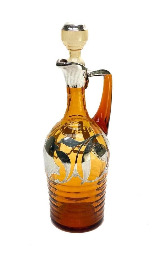Continental Silver Overlay Amber Glass Decanter. Leaf and Floral Designs: Continental silver overlay amber glass decanter. Leaf silver overlay designs and to the center with an open monogram. Ridged texture to the circular band. Polished Pontil to the underside. Weight Appr