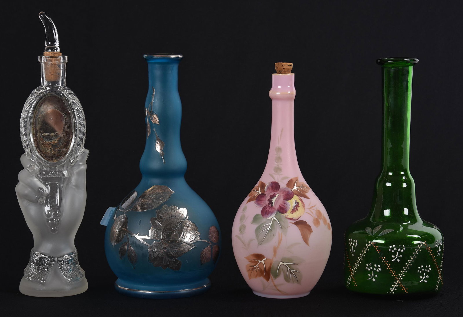 (4) Assorted art glass barber bottles: (4) Assorted art glass barber bottles; (1) 9", clear and frosted, figural hand holding mirror; (1) 7.75" blue satin with silver rose overlay; (1) 7.75" emerald green with enamel decor; (1) 7.25" pink 