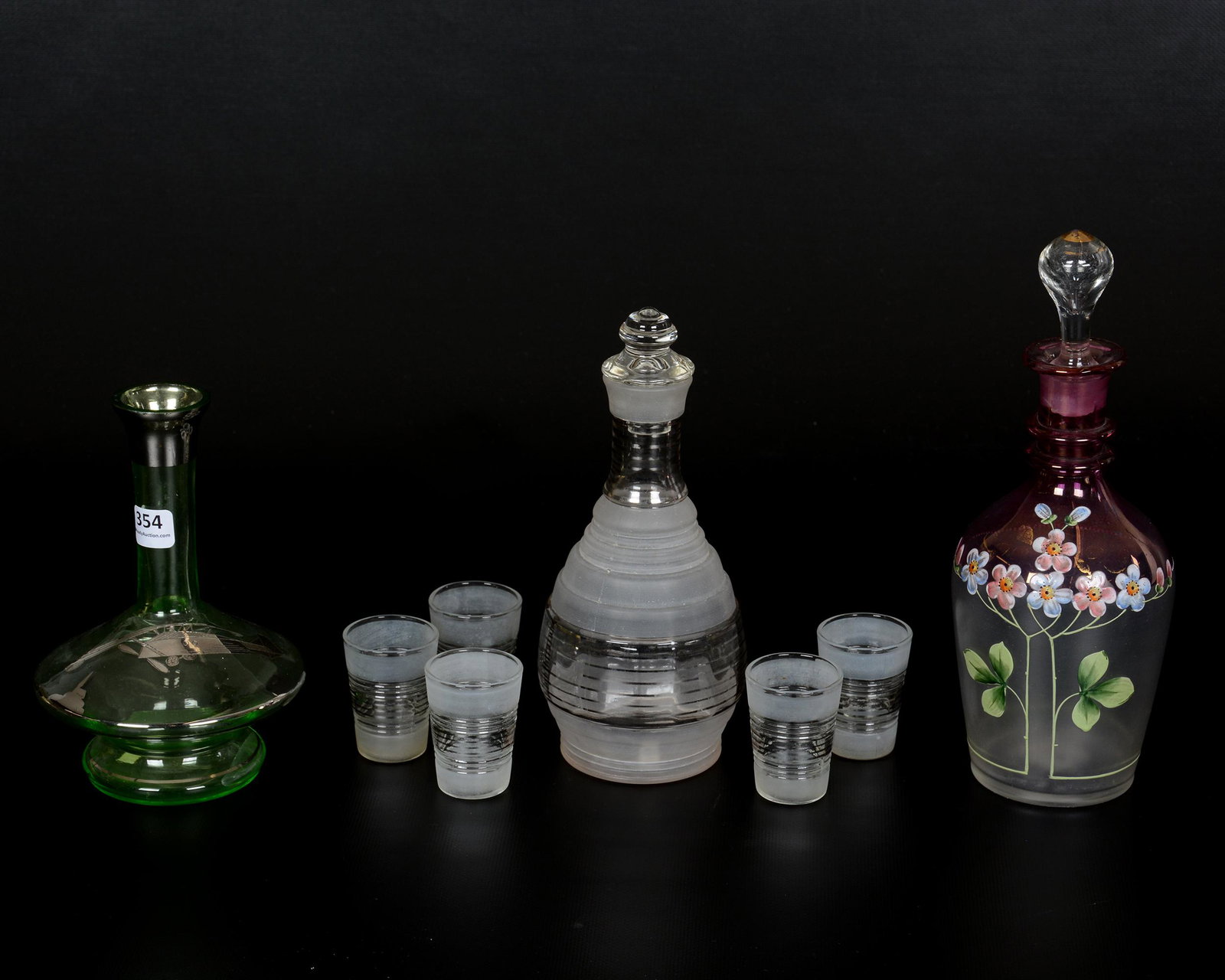 (8) Assorted Glass Decanter Items: (8) Assorted Glass Decanter Items, (1) 10" Amethyst & Frosted Decanter with Enamel Floral Decor, (1) 8.5" Frosted and Silver Threaded Decanter & (5) Matching Shot Glasses, (1) 7" Green Decanter with n
