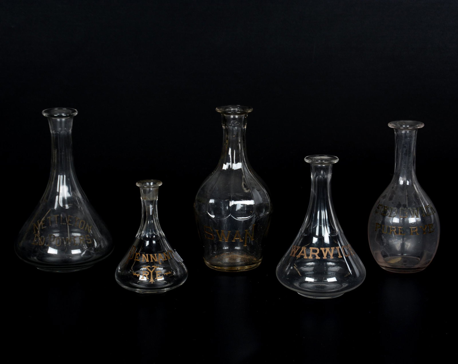 (5) Barware Advertising Decanters (No Stoppers): (5) Barware Advertising Decanters (No Stoppers), (1) 9.5" Swan; (1) 9.25" Nettleton Ed. Powers; (1) 8.5" Sedgwick Pure Rye; (1) 7.5" Warwick; (1) 6.25" Pennant Rye; the Collection of Mrs. R. and the L