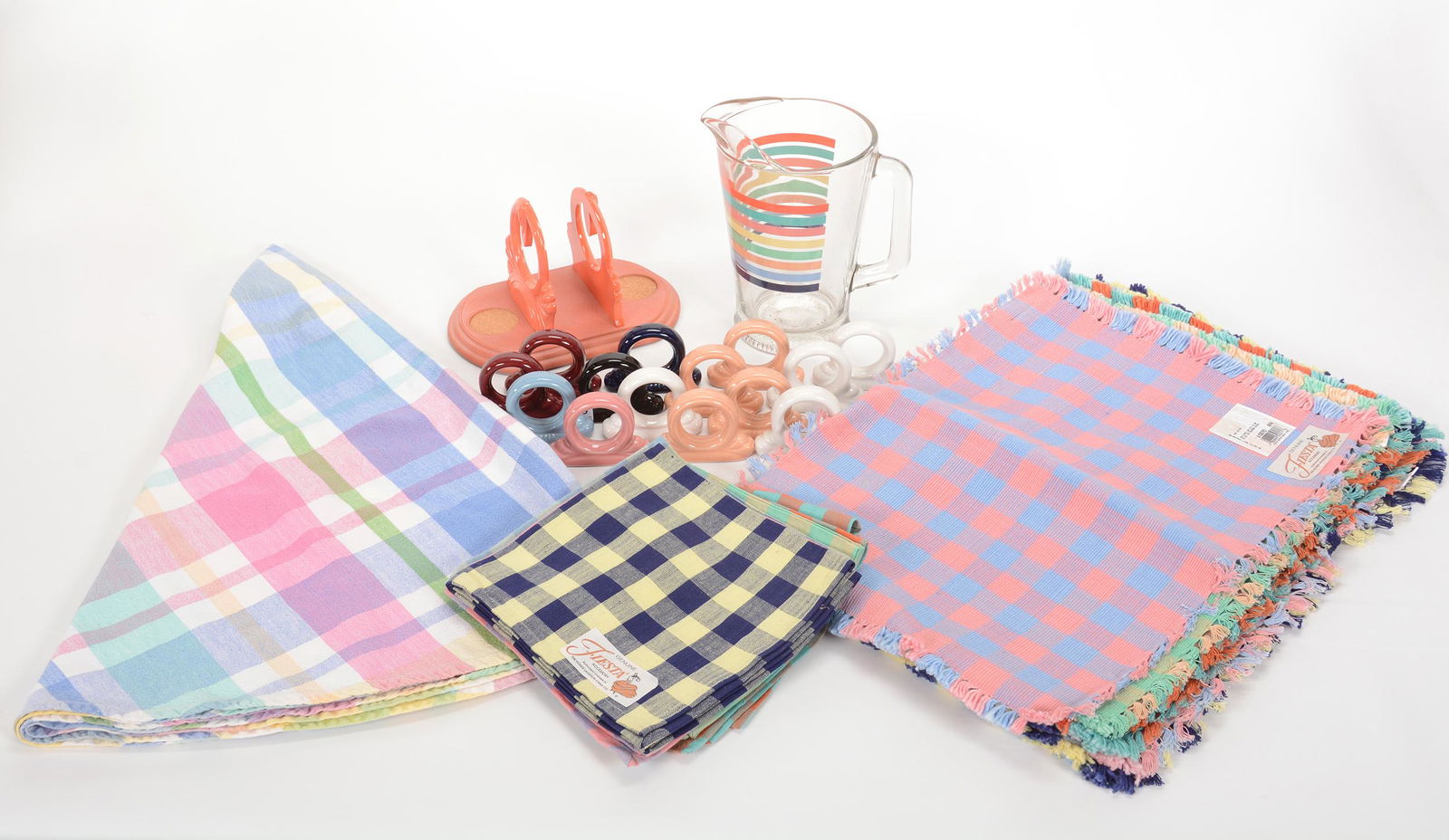 Over (24) Items Of Fiestaware Accessories: Over (24) Items Of Fiestaware Accessories, (14) Napkin Holders, One With Glaze Chip, (1) 9" Glass Fiesta Pitcher, (1) Set Of (10) Genuine Fiesta Cloth Napkins, (1) Round Cloth Table Cover In Fiesta Co