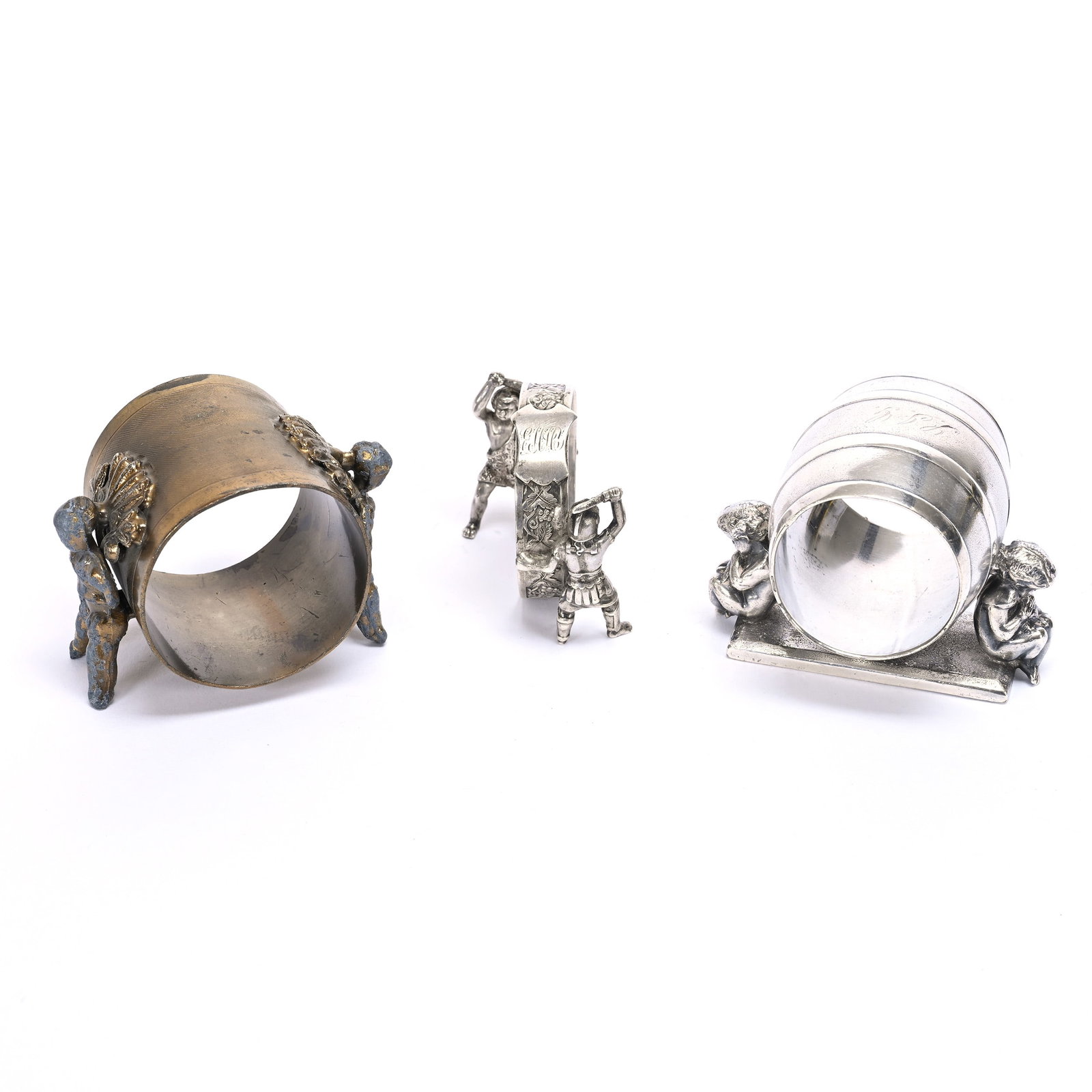 (3) Figural Napkin Rings: (3) Figural Napkin Rings, Designs With Human Figures, (1) 2.25" X 2.75", Gilded Metal, Unmarked, Some Wear, (1) 2.25" X 3", Meriden #147 Silverplate, (1) 1.75" X 2.25", Soldier With Sword & Neandertha