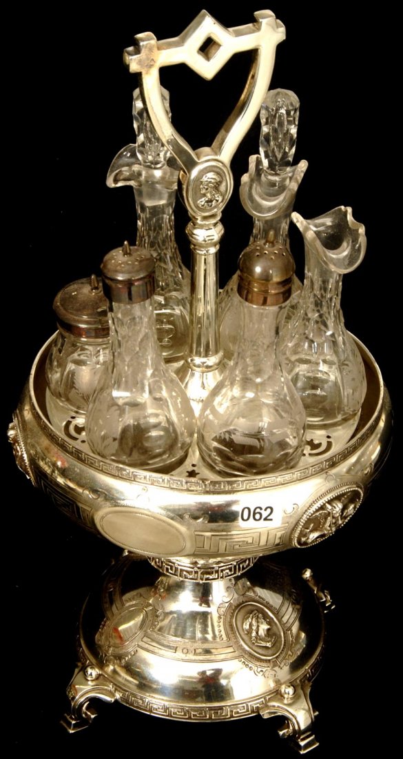 16 1/2" SIX BOTTLE CASTOR SET ON FANCY SILVER PLATE: 16 1/2" SIX BOTTLE CASTOR SET ON FANCY SILVER PLATE FRAME CLEAR BOTTLES W/ ETCHED LEAF DECOR (one cruet missing stopper) - EMBOSSED CHERUB RIDING DOLPHIN SCENIC DECOR