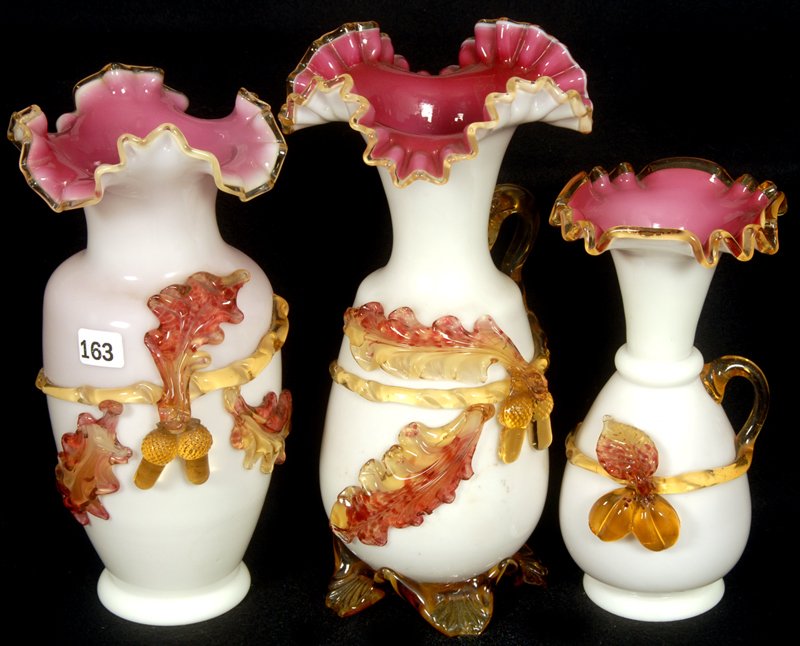 (3) STEVENS & WILLIAMS ART GLASS CASED ITEMS: (3) STEVENS & WILLIAMS ART GLASS CASED ITEMS WHITE W/ PINK INTERIORS & APPLIED AMBER ACORN & FRUIT DECOR - (1) 10" HANDLED EWER W/ PETAL FEET (some w/ minor chips); (1) 9 1/2" VASE - (1) 7 3/4" HANDLE