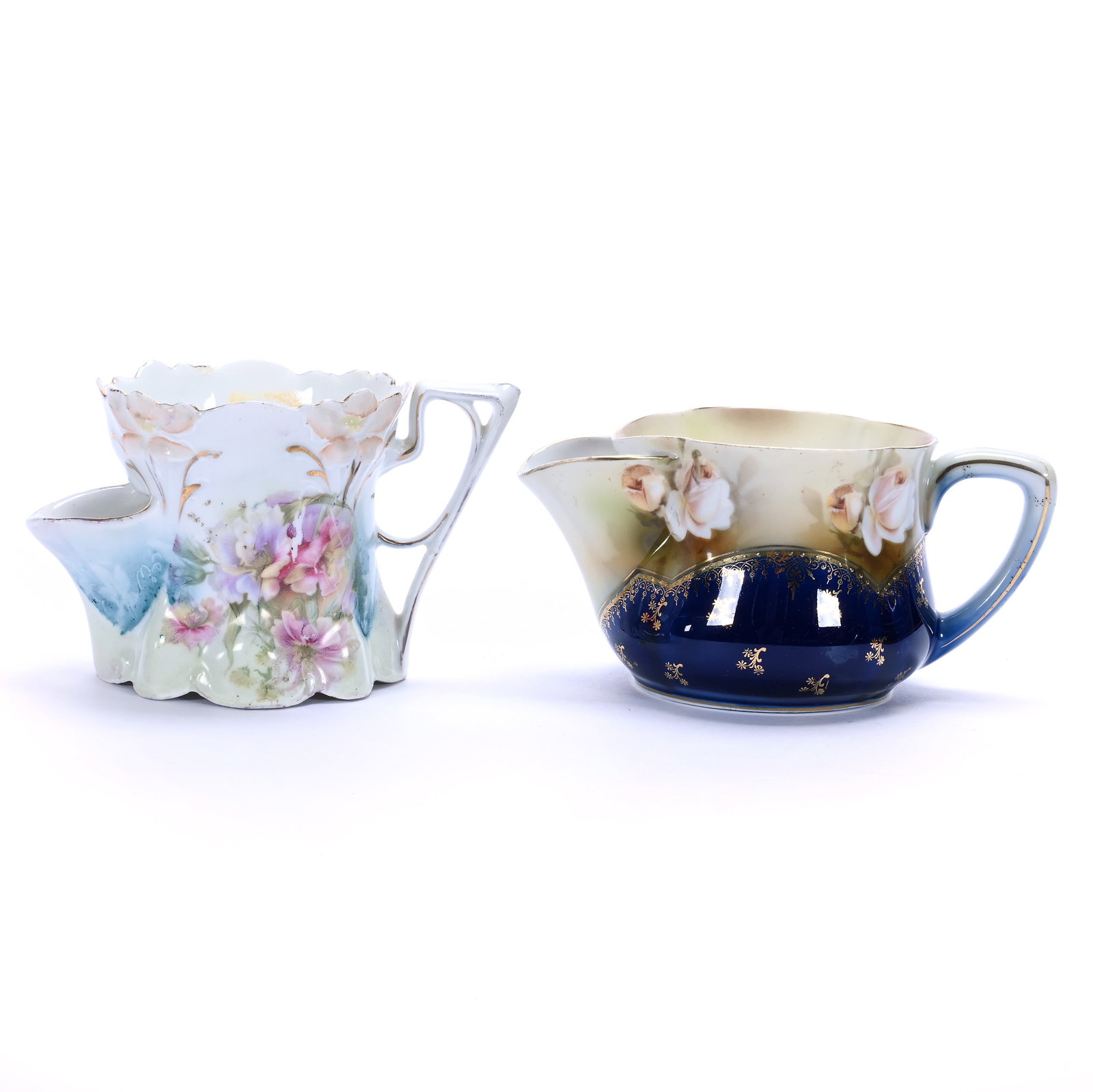 (2) Scuttle Mugs, Unmarked R.S. Prussia: (2) Scuttle Mugs, Unmarked R.S. Prussia, 3.5 x 5.5 x 3.25 Inches, Floral Decor, (1) Lily Mold, Blue, Green, And White Tones, Rim Chip, (1) Marked R.S. Germany, Cream And Cobalt Blue With Pink Rose