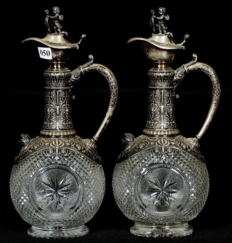 PAIR ENGLISH CUT GLASS HANDLED EWERS - 12": PAIR ENGLISH CUT GLASS HANDLED EWERS - 12" OVOID SHAPE WITH DIAMOND POINT CUT BODY AND CIRCULAR STARBURST MEDALLION - ELABORATE EMBOSSED SILVER FITTINGS WITH CHERUB FINIAL - CHERUBS ARE HOLDING MONOGR