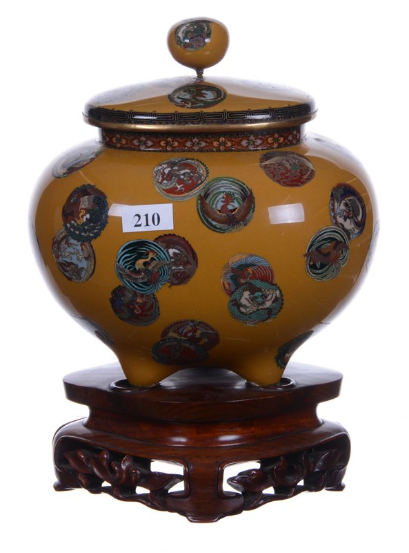 7" X 7" CLOISONNE OVOID THREE FOOTED COVERED URN: 7" X 7" CLOISONNE OVOID THREE FOOTED COVERED URN GOLD BACKGROUND WITH INTRICATE AND COLORFUL DRAGON AND PHOENIX MEDALLIONS - MATCHING LID AND FINIAL - GOLD STONE BORDER - SET ON 2.5" TALL CARVED TEAK