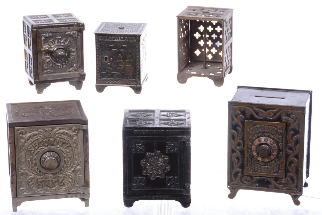 (6) CAST IRON STILL BANKS - VARIOUS DESIGNS: SIZES RANGE FROM 3.5" TO 6" - (1) "THE ROLLER SAFE" FEATURING PEOPLE ON ROLLER SKATES DATED 1882 - (1) "IDEAL SAFE DEPOSIT" - (1) "SECURITY SAFE" WITH FLAG AND FIREARM DESIGN - AND MORE - SEE PHOTOS F