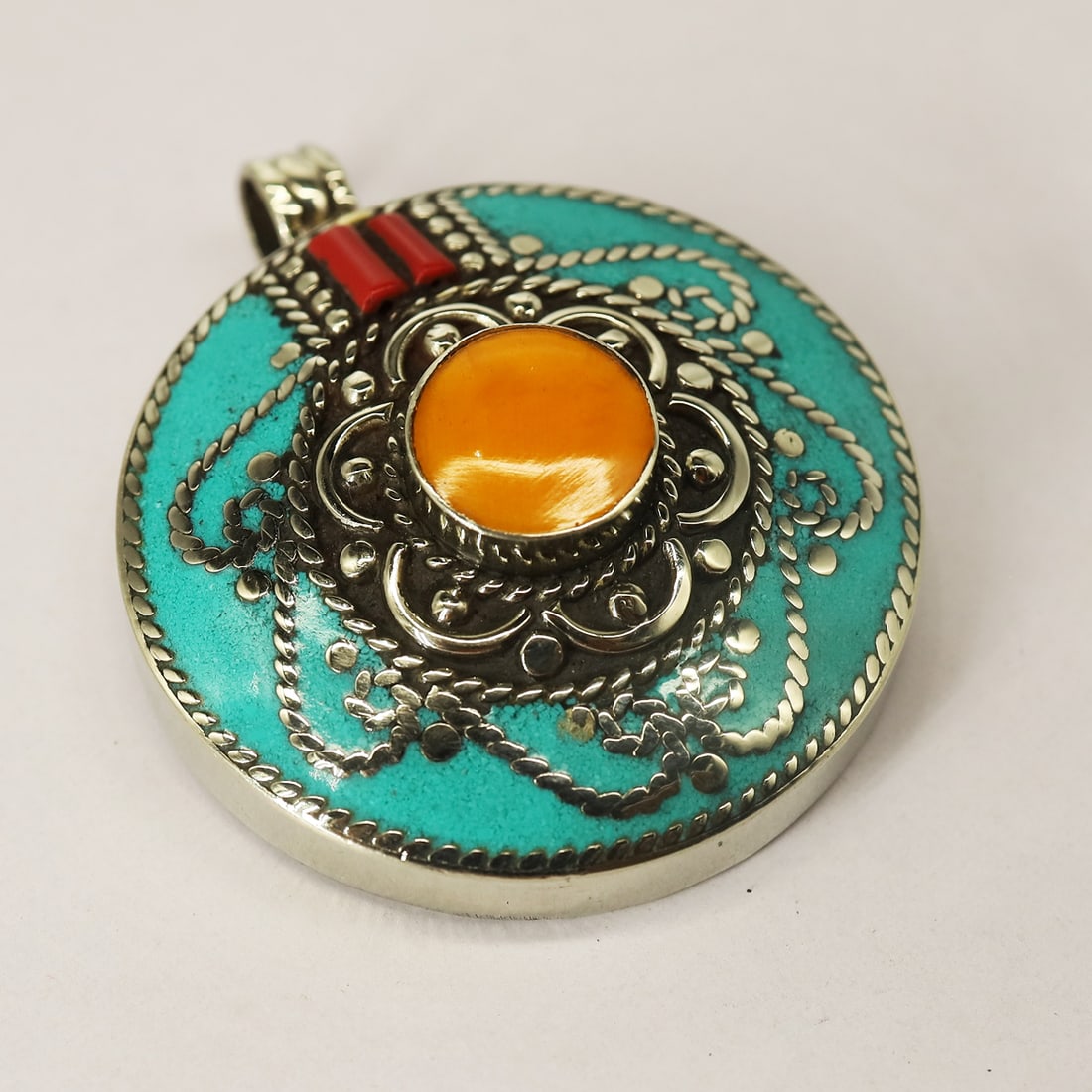 Tibetan Turquoise & Copal Handmade Pendant: Product ID: 250804180122Product - Tibetan Handmade PendantSize - 4.2X4.2 CM RoundWeight - 41 GramMetal - Brass & Copper mix MetalOrigin - Nepal Country/Region of Manufacture - Nepal At Your Service: A