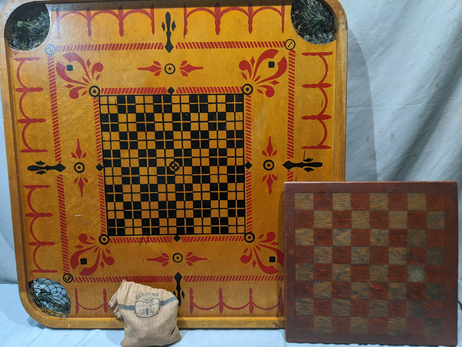 Lot 2 Antique Game Boards Carroms & Checker Board: Double sided Carroms game with 34 wooden game pieces in original printed cloth pouch along with a country style checkers board. Measurements in inches: 28 1/2 x 28 3/4 and 13 1/2 x 14 Condition:Carrom