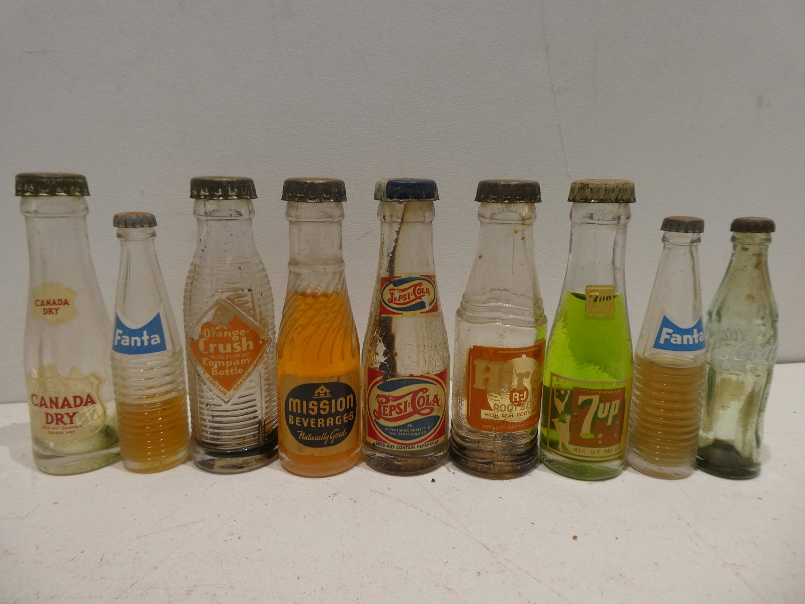 Lot 9 Vintage Miniature Glass Soda Pop Sample Bottles: Lot 9 Vintage Miniature Glass Soda Pop Sample Bottles including Pepsi, Coke, 7up, Mission, Crush, Canada Dry, Fanta and Hires. Condition:Has some wear in labels Shipping:We offer in-house shipping. It