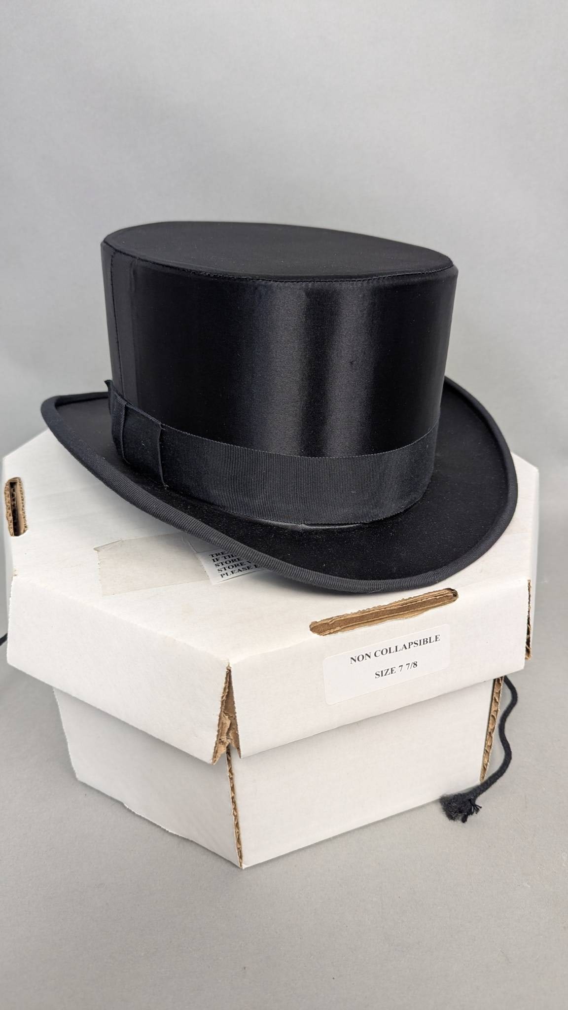 DelMonico Satin Top Hat in Black, Size 7 1/8 with Hatbox: A DelMonico Satin Top Hat, size 7 1/8, in black with classic satin construction and grosgrain ribbon detail. Made in the USA by Hats of America, Inc. Includes the original hatbox.. Condition:Well take