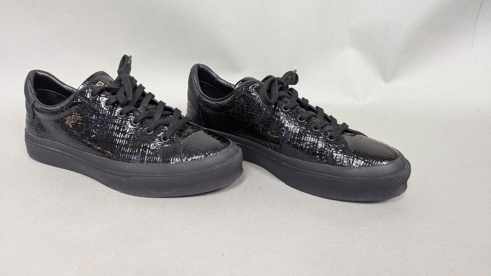 Givenchy Black Patent Leather Low-Top Sneakers, Size 44: Givenchy black low-top sneakers crafted from patent leather with a textured geometric pattern. Features lace-up closures, rubber soles, and branded heel tabs. The insole is branded with the Givenchy l