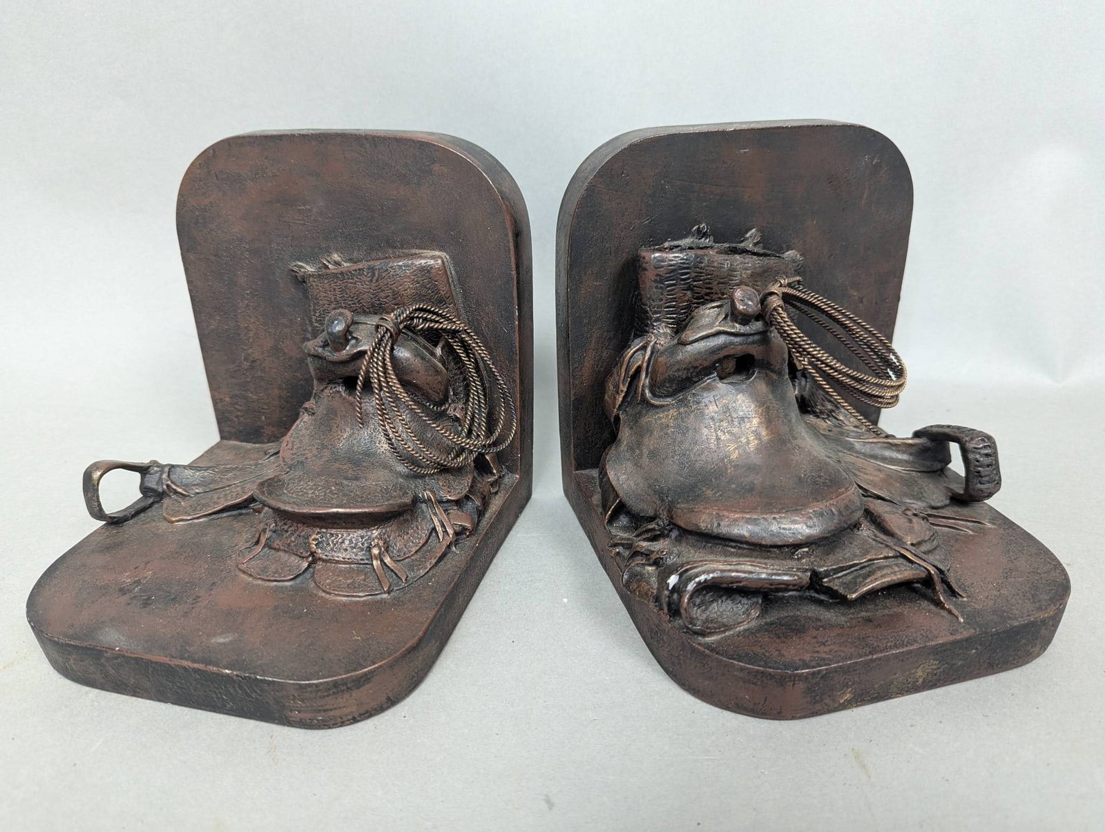 Western Moments Cowboy Horse Saddle Bookends: A pair of Western Moments bookends featuring detailed designs of saddles with metallic rope accents. Each bookend measures 6 inches high, 6 inches wide, and 6 inches deep. Made of resin with a rustic 