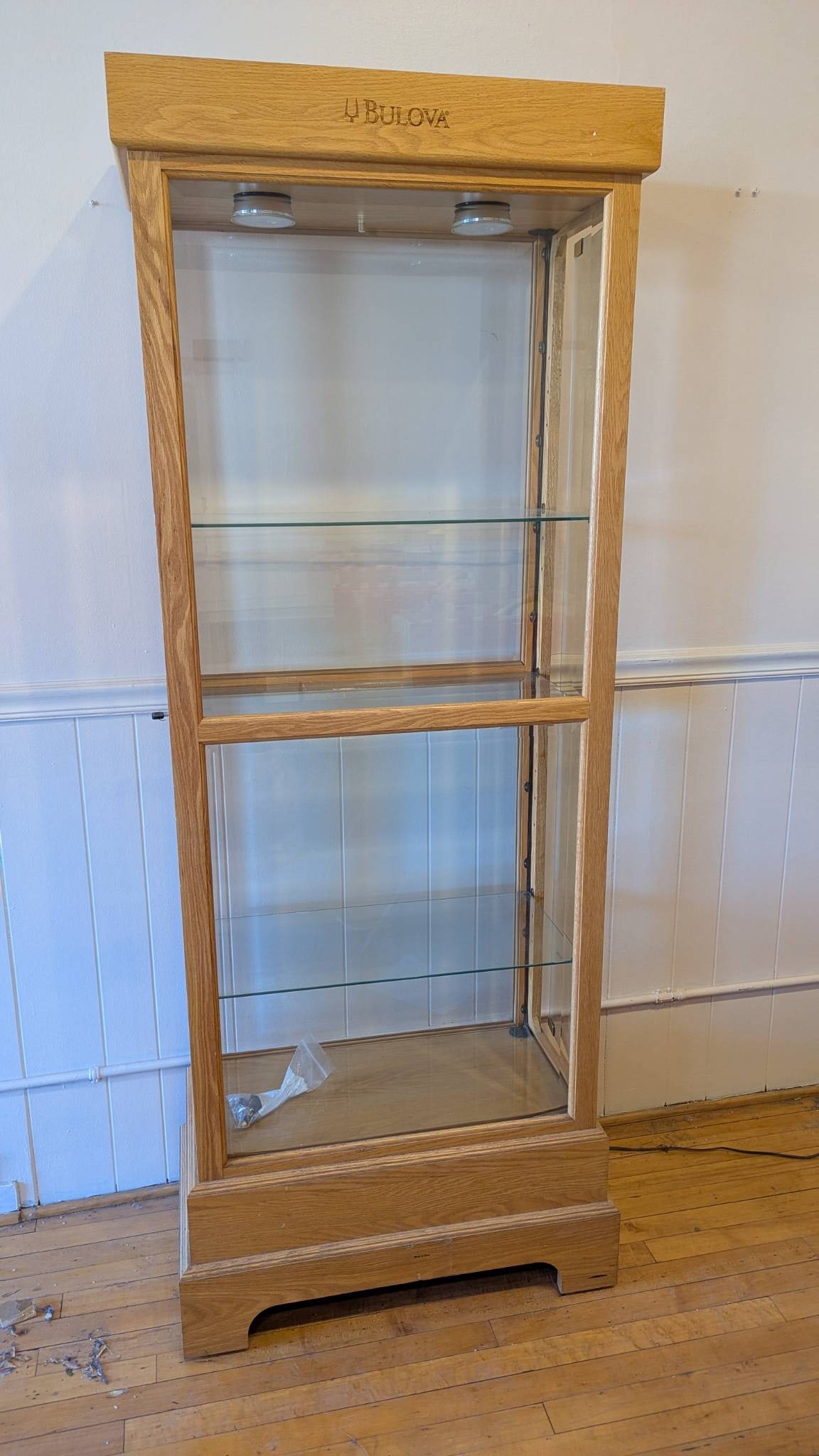 Bulova Wood and Glass Display Cabinet with Shelves and Lighting: Bulova branded display cabinet measuring 76.5 inches high, 29 inches wide, and 15 inches deep. Constructed of wood with glass panels and featuring two adjustable glass shelves. Includes built-in light