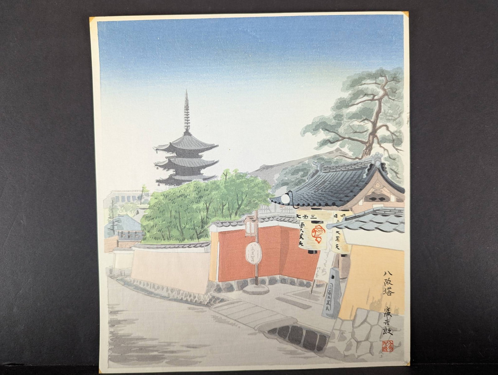 Japanese Woodblock Print Pagoda at Yasaka by Tomikichiro Tokuriki: Japanese woodblock print titled Pagoda at Yasaka from the Twelve Months of Kyoto series by artist Tomikichiro Tokuriki (1902-2000). Created circa 1950s, this artwork features a serene depiction of a t