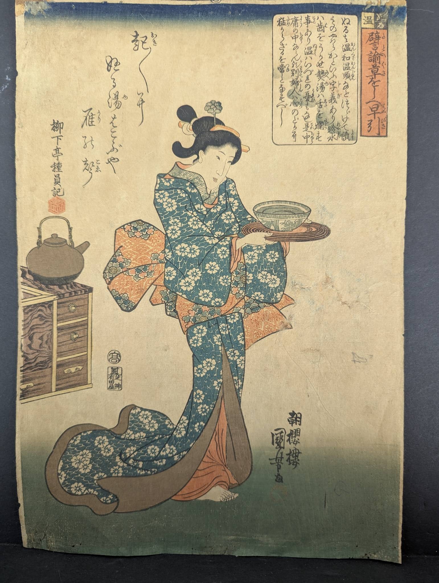 Japanese Woodblock Print Featuring Geisha Holding Bowl by Kunisada: Japanese woodblock print attributed to artist Utagawa Kunisada, also known as Toyokuni III. The artwork depicts a geisha dressed in an elaborate floral kimono, holding a bowl on a tray. Elements such 