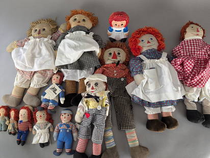 Collection of Raggedy Ann and Andy Dolls in Various Sizes and Styles: A collection of Raggedy Ann and Andy dolls featuring various sizes, materials, and styles. Included are several cloth dolls with traditional red yarn hair and embroidered details, some of which are