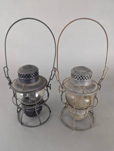 Pair of New York Central Railroad Lanterns Marked NYC and Adlake Kero: A pair of Adlake Kero railroad lanterns, both marked with NYC on the top, possibly indicating New York Central. Both lanterns feature metal cages and glass globes, with one showing a darker patina